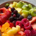 Colorful bowl of fresh fruit salad with various fruits like berries, melons, and kiwi.