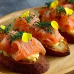 Smoked salmon crostini topped with cream cheese and herbs on a wooden board