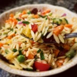 A colorful orzo salad with fresh vegetables and herbs served in a bowl.