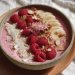 Pink raspberry smoothie bowl topped with fresh fruits and granola
