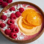 Delicious Raspberry Orange Smoothie Bowl topped with fresh fruits and nuts.