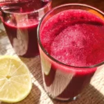 Freshly prepared beet juice in a glass with beets and greens in the background.