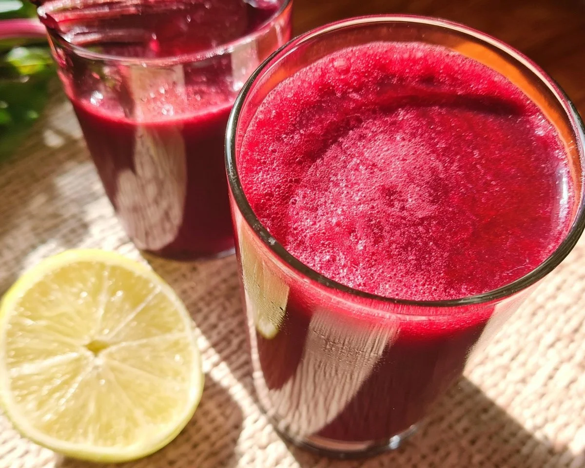 Freshly prepared beet juice in a glass with beets and greens in the background.