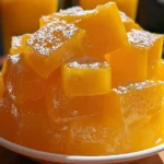 Wobbly cubes of mango jelly served in a bowl, showcasing vibrant orange color.