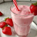Fresh strawberry banana smoothie in a glass with a straw and fresh fruit